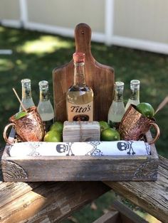 a wooden tray with bottles and glasses in it sitting on top of a picnic table