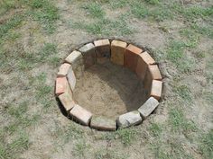 a brick fire pit sitting in the middle of a grass covered field with dirt on it