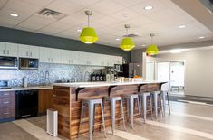 an open kitchen with bar stools and yellow lights hanging from the ceiling above it