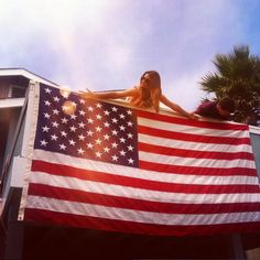 a woman holding an american flag on top of a building