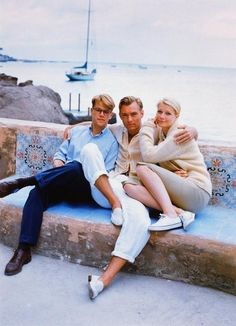 two people are sitting on a bench near the water and one person is holding his arm around the woman's shoulder