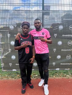 two young men standing next to each other in front of a fence with a backdrop