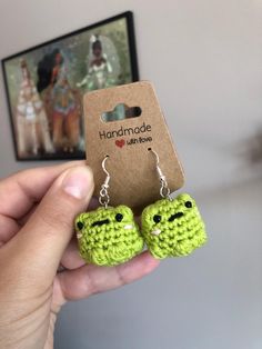 a pair of green crocheted frog earrings with black eyes are shown in front of a photo