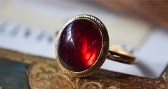 The Classic Dragon Breath Vintage Ring features a mesmerizing deep red garnet stone that captures the light with every turn. Set in a classic gold band with delicate beaded detailing, this ring exudes a timeless elegance. The rich crimson hue of the garnet adds a bold pop of color, making it a striking accessory for any occasion. Perfect for those who appreciate vintage-inspired pieces with a modern twist, the Classic Halo Vintage Ring is designed to enhance your look with a touch of sophistication and charm. Details Classic Halo Vintage Ring in Red Gold pleated Adjustable opening Missy Jewelry Dragon Breath Collection Classic Red Ruby Ring, Oval Cabochon, Classic Red Ruby Ring With Oval Cabochon, Timeless Red Ring As A Gift, 14k Gold Red Cabochon Ring, 14k Gold Cabochon Red Ring, Timeless Red Ruby Ring, Classic Burgundy Ruby Ring, Timeless Red Gemstone Jewelry, Red Ruby Oval Cabochon Ring In 14k Gold