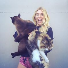 a woman holding two cats in her arms and making a funny face at the camera