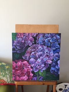 an easel with a painting of purple flowers on it and a green pillow next to it