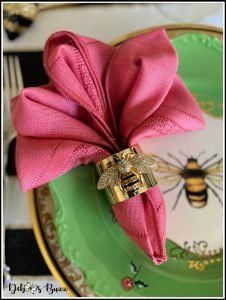 a pink napkin on top of a green plate with a gold bee and honey comb