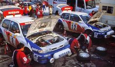 men working on cars in a parking lot with other vehicles and people looking at them