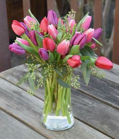 a vase filled with pink and purple tulips on top of a wooden table