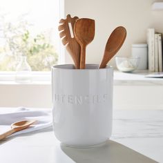 three wooden spoons in a white cup with utensils