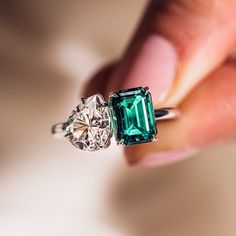 a woman's hand holding an emerald and diamond ring