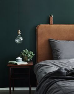 the bed is made with dark green walls and grey linens, along with a brown leather headboard