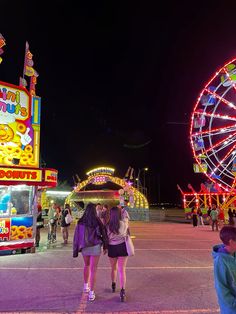 two girls standing in front of an amusement park ride at night with ferris wheel and carnival rides behind them