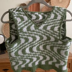 a green and white knitted sweater hanging on a wooden rack next to a clock