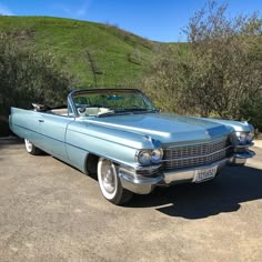 an old blue car is parked on the side of the road in front of some bushes