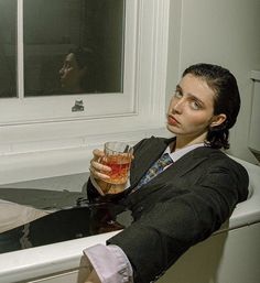 a woman sitting in a bathtub holding a drink