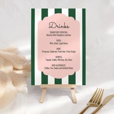 a pink and green striped menu card on a wooden easer with gold forks next to it