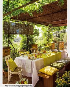 an outdoor dining area with yellow and white table cloths, green cushions, and greenery