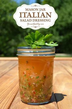 a mason jar filled with salad dressing sitting on top of a wooden table next to trees