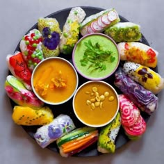 colorful sushi rolls with dipping sauces on a black plate next to other food items