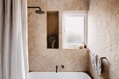 a bath tub sitting under a window next to a shower curtain and a towel rack