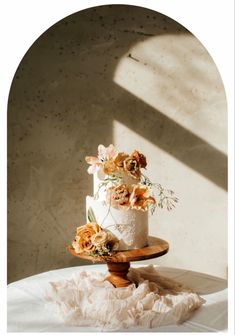 a three tiered wedding cake with fresh flowers on top sits on a wooden stand