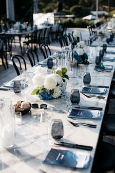 the table is set with silverware and white flowers in vases on each side