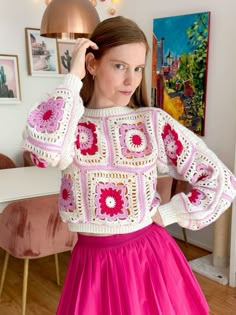 a woman in a pink skirt is wearing a crocheted sweater with flowers on it