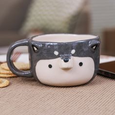 a ceramic mug with a bear's face on it sitting next to crackers