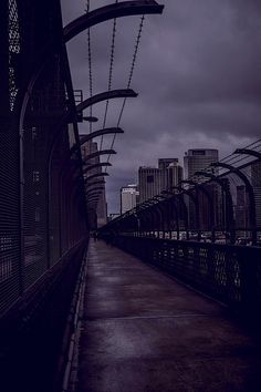 an empty walkway in the middle of a city with tall buildings on either side and dark clouds overhead