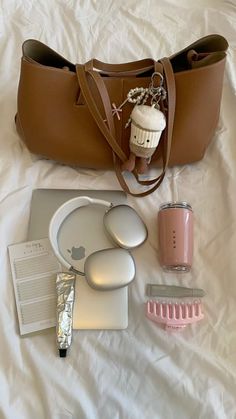 the contents of a handbag laid out on a bed next to an apple laptop