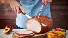 a person cutting up a ham on top of a wooden board next to sliced peaches