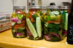 four mason jars filled with pickles, cucumbers and other veggies