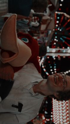 a man with glasses and a red mask holding onto a stuffed animal in front of christmas lights