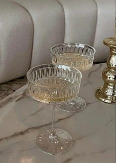 two clear wine glasses sitting on top of a marble table next to a gold candle holder