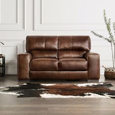 a brown leather couch sitting on top of a wooden floor next to a white wall