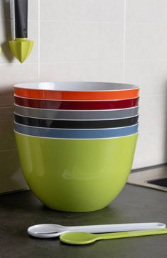 a stack of colorful bowls sitting on top of a kitchen counter next to a knife