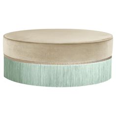 a round ottoman with fringe trim around the top and bottom in beige, mint green and white