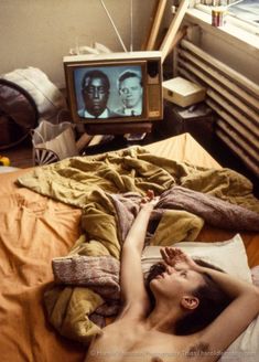 a shirtless man laying on a bed in front of a tv