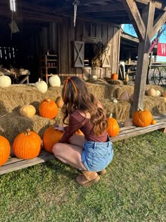 a woman kneeling down next to hay bales filled with pumpkins