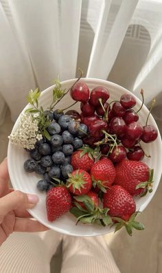 a white bowl filled with strawberries and blueberries on top of a table next to a window