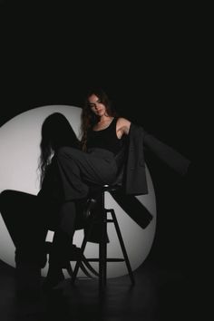 a woman sitting on top of a stool in front of a white ball and black background