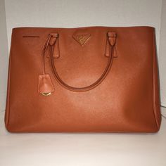 Prada Safiano Lux Rame Tote Bag Color: Rame, A Deep Rust Like Orange, The Color Is Absolutely Beautiful Bn1844 Nzv P0126 00 P101 2012 08698 C Condition: New With Tag Comes With Tag & Dust Bag This Classic Shape In Soft, Stamped Leather Has Radiant Hardware, Including A Front Logo Embellishment. Double Top Handles, 5" Drop Magnetic Clip Closure Saffiano Leather Triangle Logo With Metal Lettering One Inside Zip Pocket Three Inside Open Slip Pocket Protective Metal Feet Prada Logo Lining 15"W X 10" Brown Saffiano Leather Bags With Handles, Designer Brown Saffiano Leather Bag, Designer Brown Saffiano Leather Satchel, Cognac Saffiano Leather Bag With Double Handle, Brown Saffiano Leather Bag With Removable Pouch, Elegant Cognac Saffiano Leather Bags, Brown Saffiano Leather Rectangular Bag, Luxury Saffiano Leather Satchel For Shopping, Prada Bag Saffiano