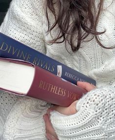 a woman is holding two books in her hands while wearing a white knitted sweater