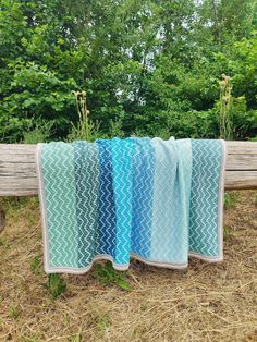 three blue and white crocheted blankets on a wooden bench in front of trees