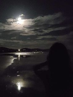 a woman standing on the beach at night with her back to the camera, looking into the distance