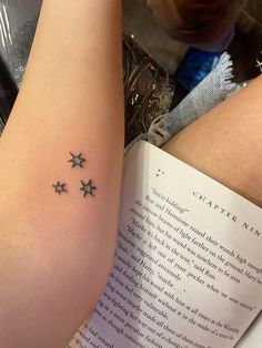 a woman's arm with three stars on it and an open book in the background