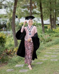 a woman wearing a graduation gown and holding a cell phone to her ear while walking down a path