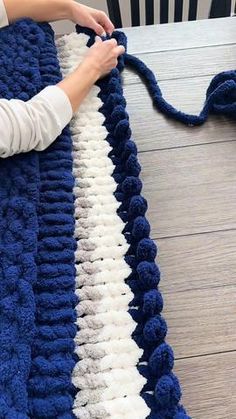 someone is crocheting a blue and white blanket on the floor with yarns