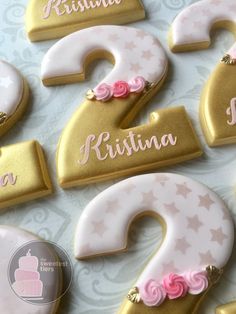 decorated cookies with pink and gold icing are displayed on a white tableclothed surface